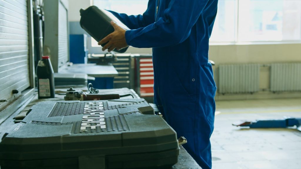 pexels-photo-8985459 Mechanic in blue overalls holding engine oil container in a workshop environment, enhancing maintenance efficiency.